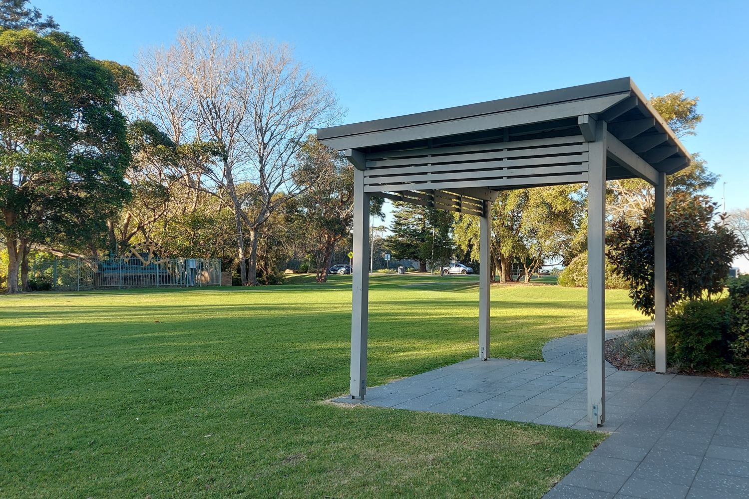 Grassy space to the north of the building, with a pergola and paved path in the foreground.