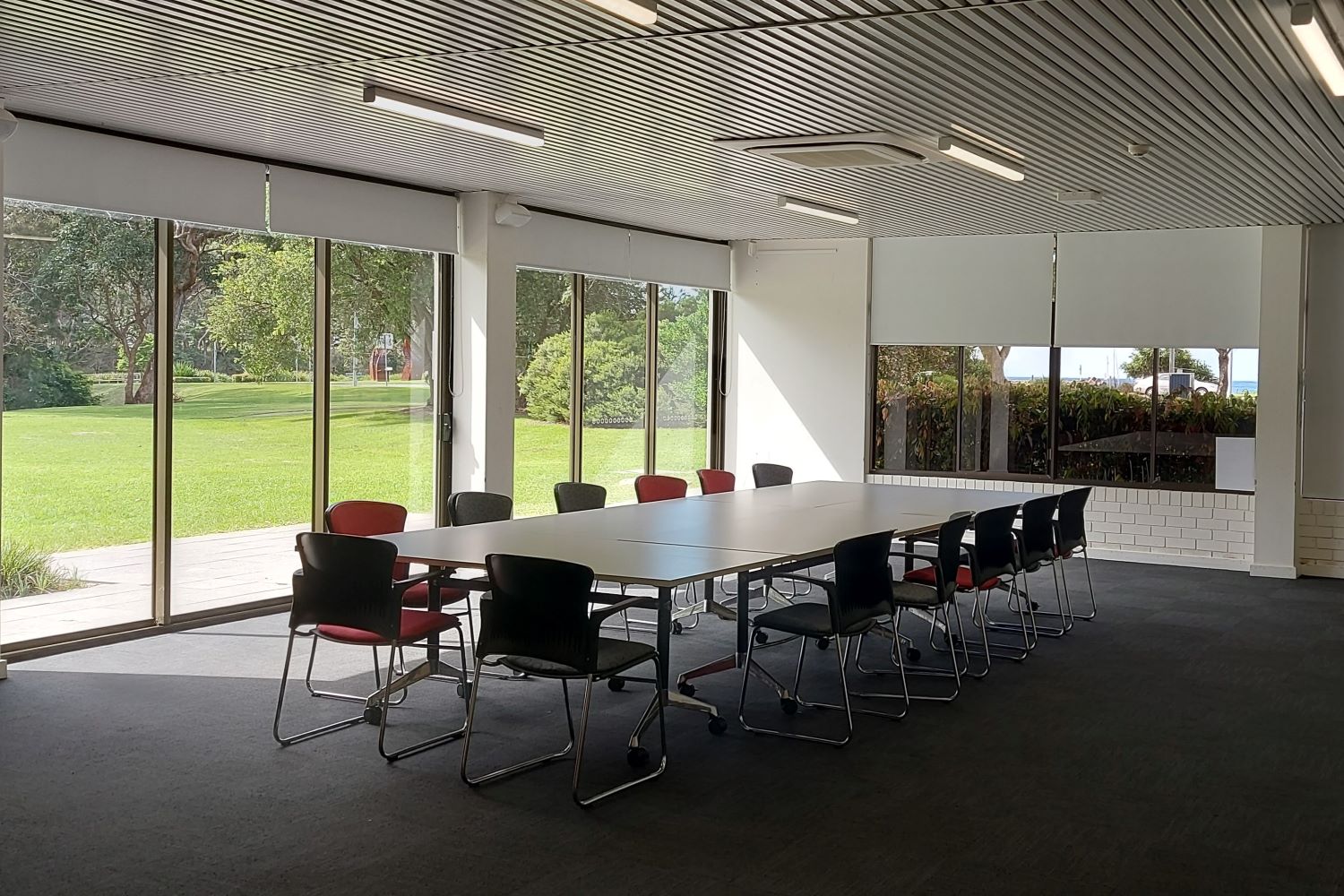 Large rectangular boardroom table in ground floor room with floor to ceiling glass doors onto grass and grounds.