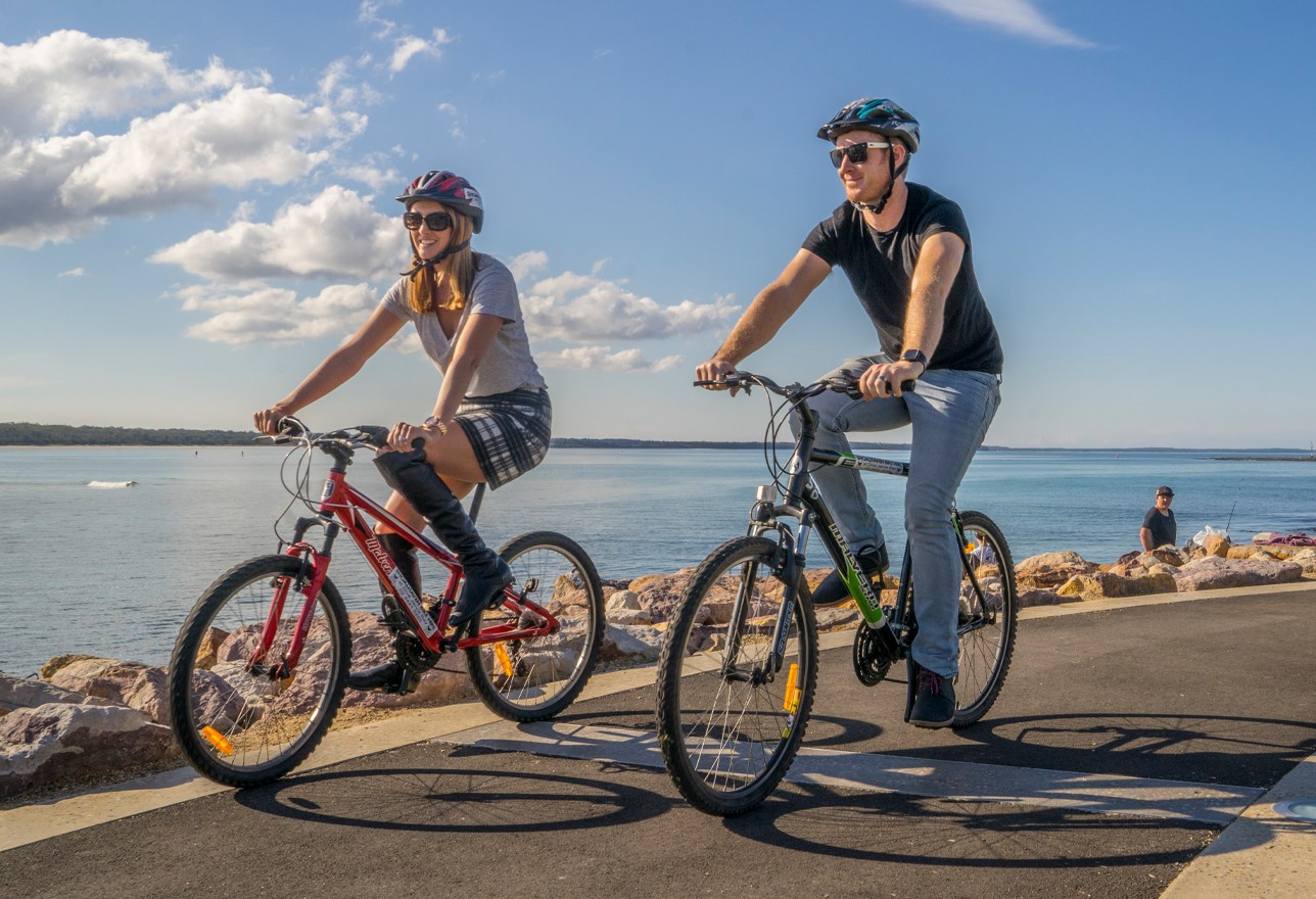 Two people riding push bikes along a footpath 