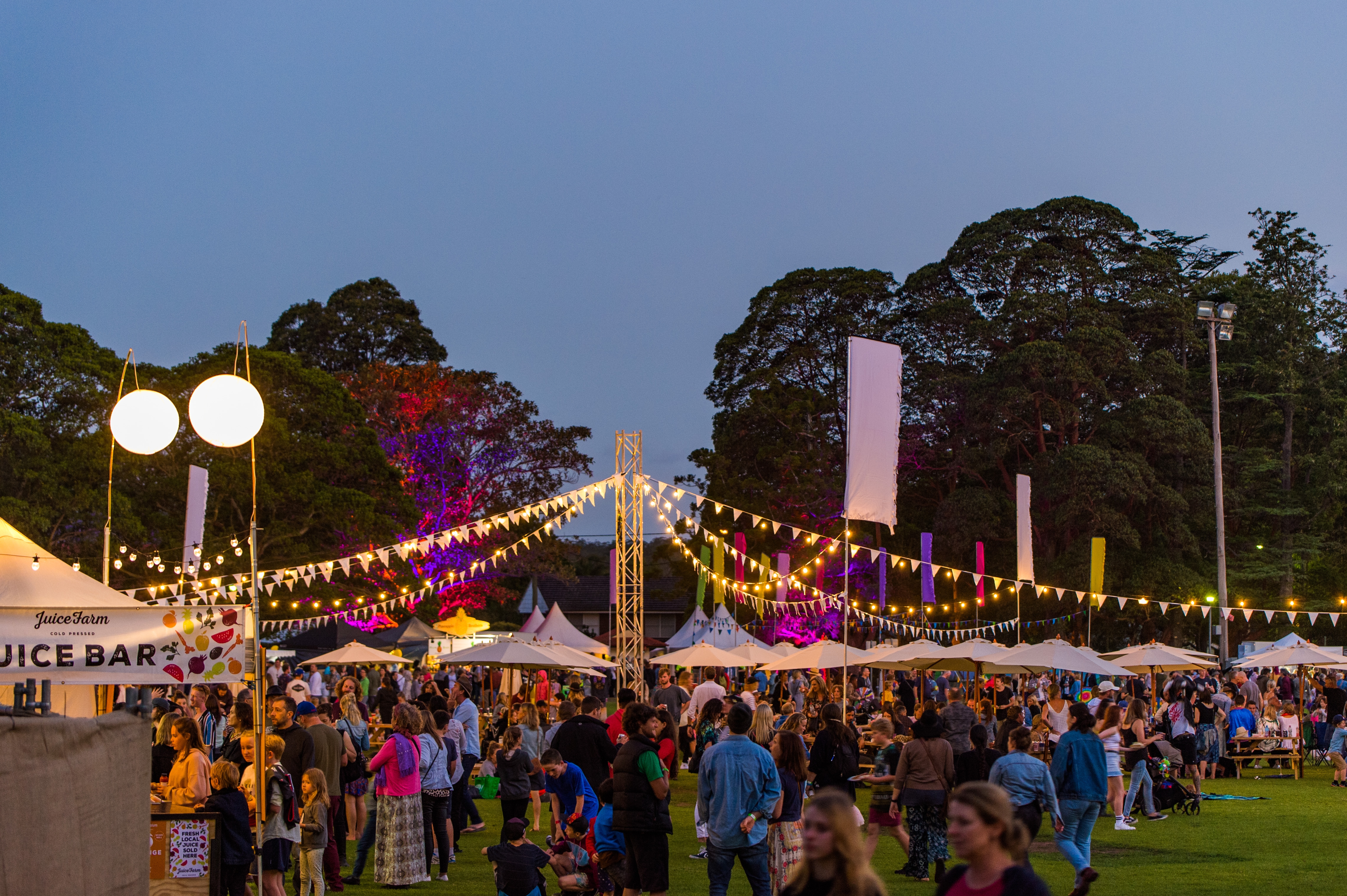 A crowd of people at a festival with banners and lights.