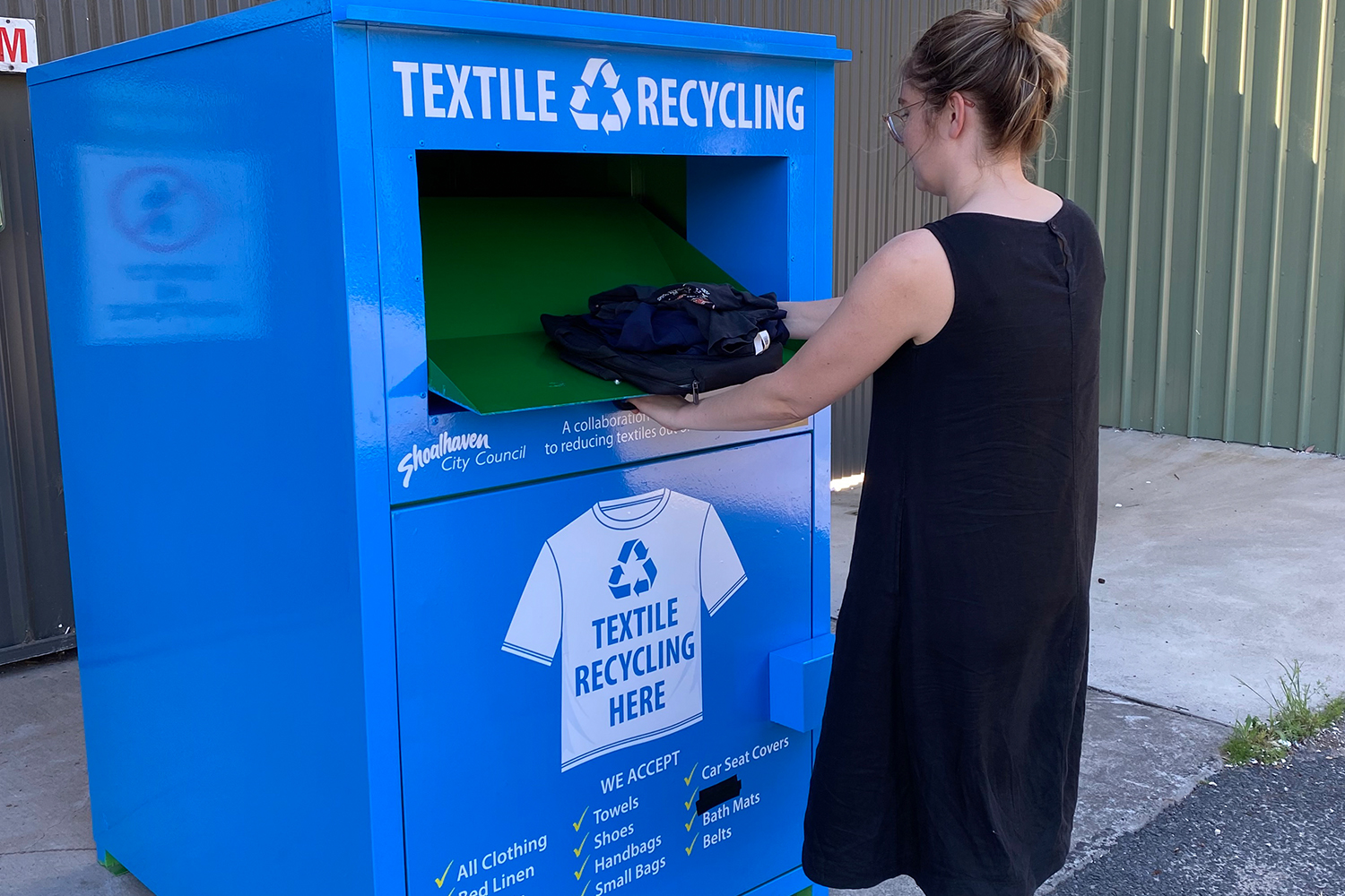 A person putting old textiles into the large textile recycling bin at a depot